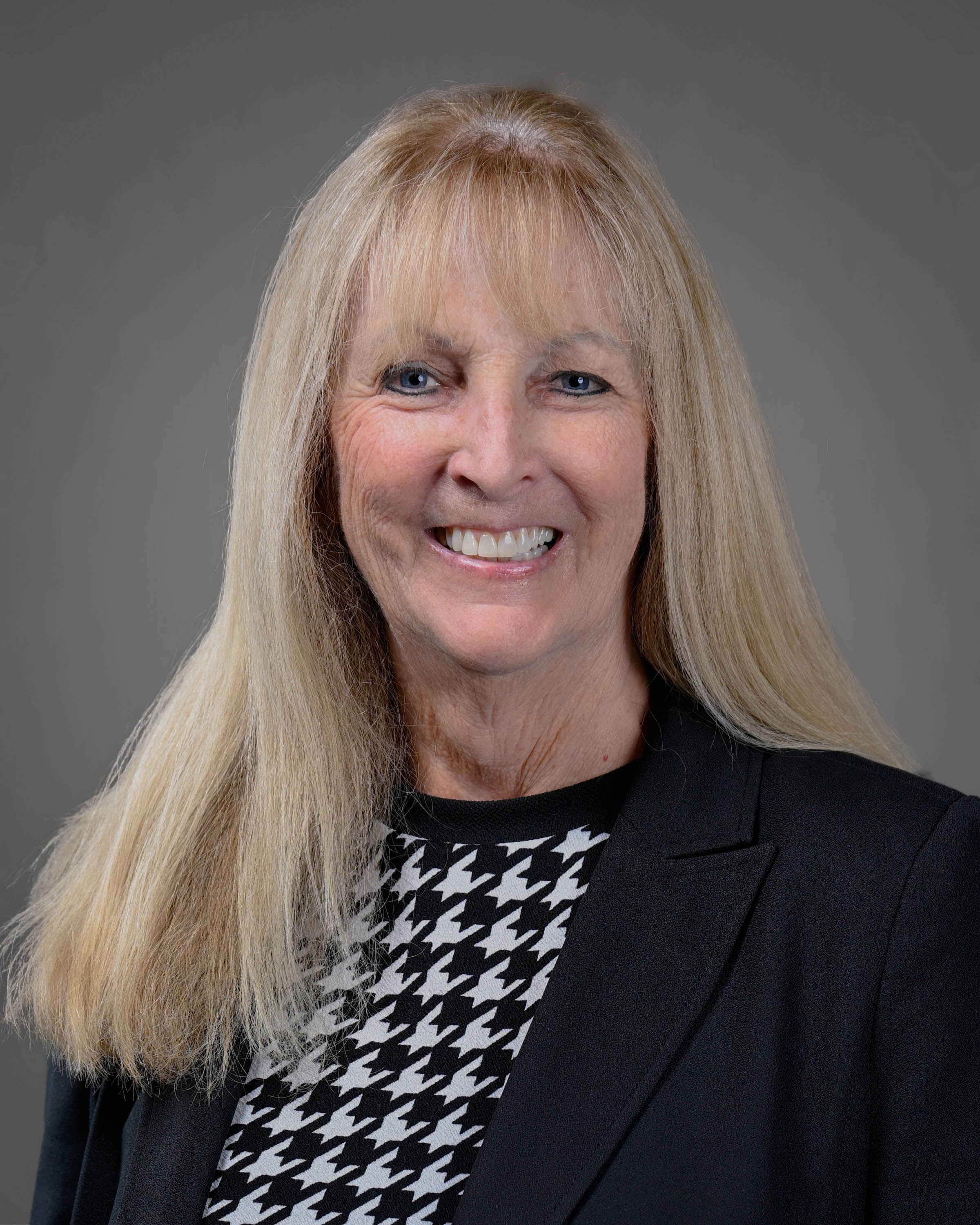 Smiling blonde woman in a dark suit jacket with a white and black shirt.
